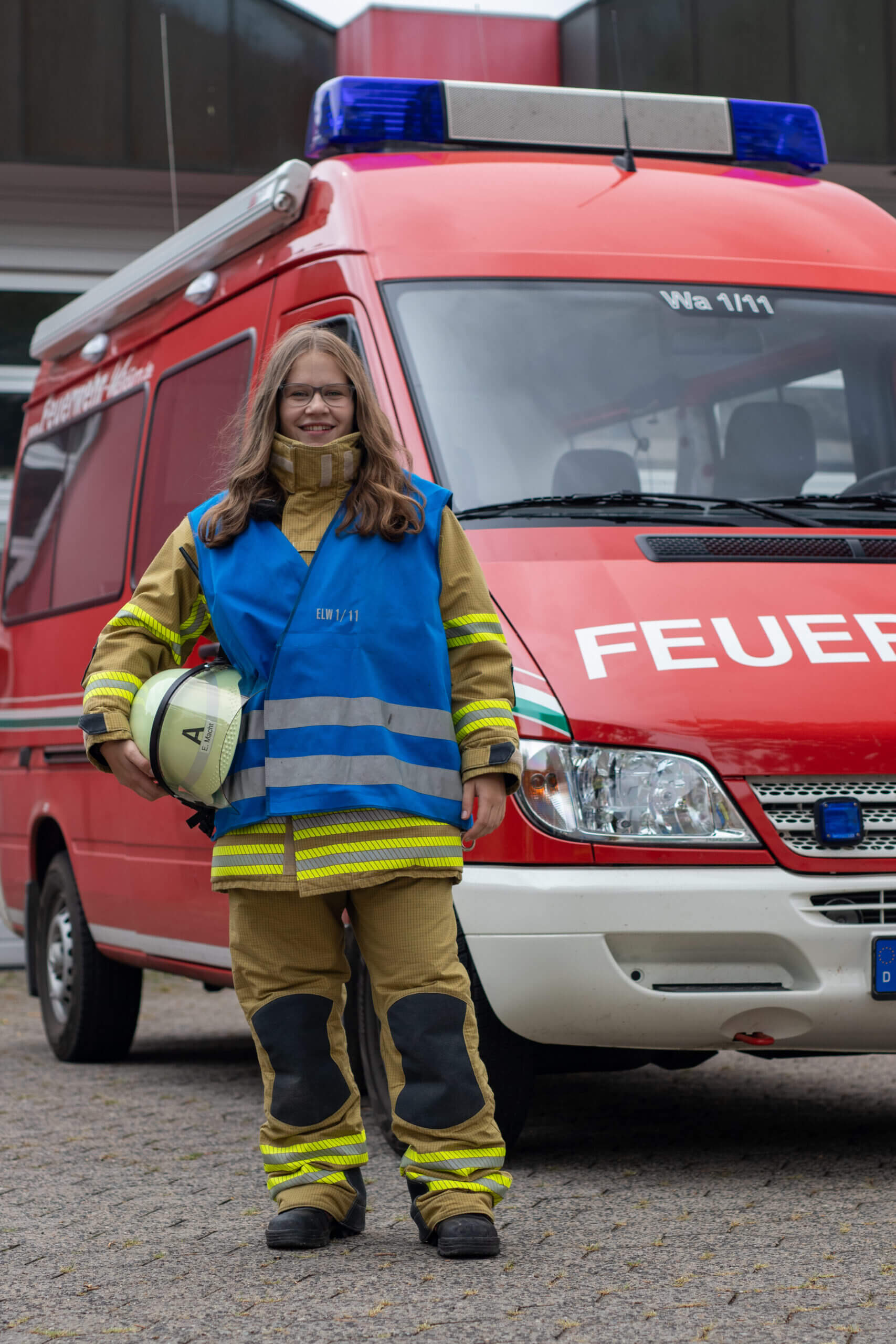 Feuerwehrfrau mit einer blauen Funktionswesten vor dem Einsatzleitwagen.